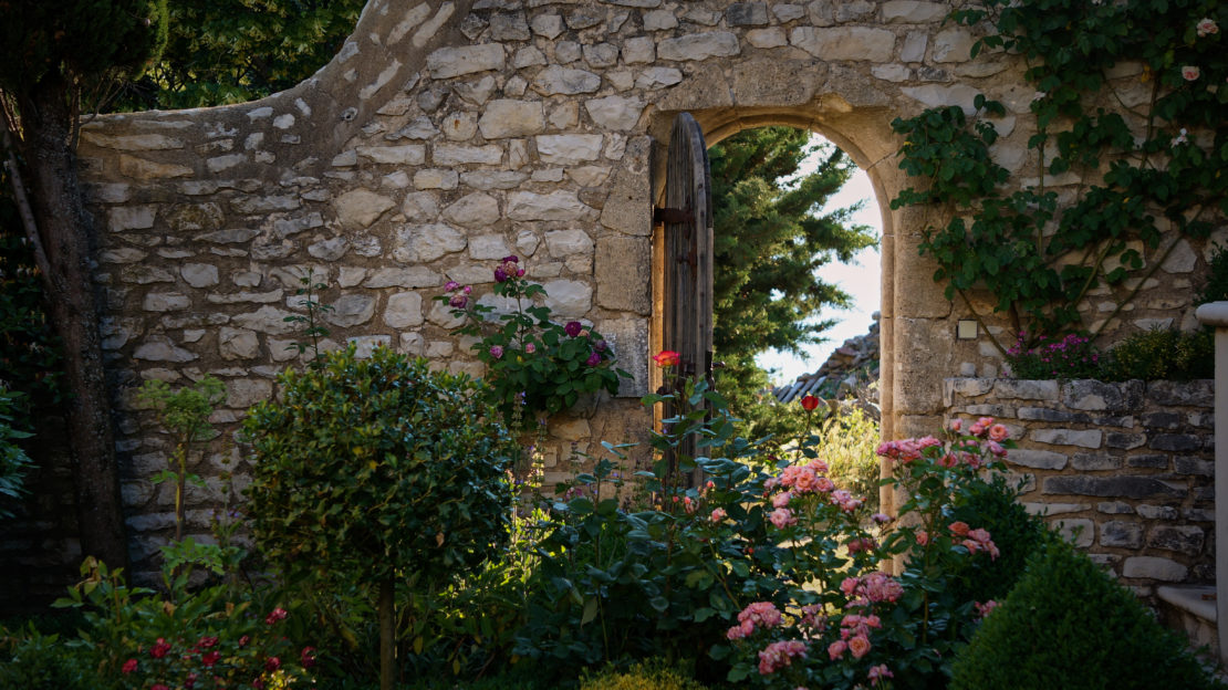 a stone wall with an open gate in a pretty enchanted garden