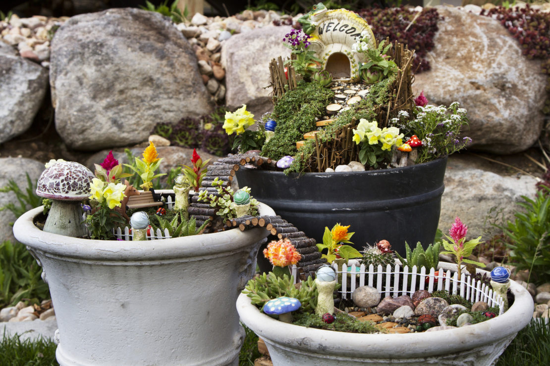 Three pots with miniature fences, flowers and doorways, creating fairy gardens