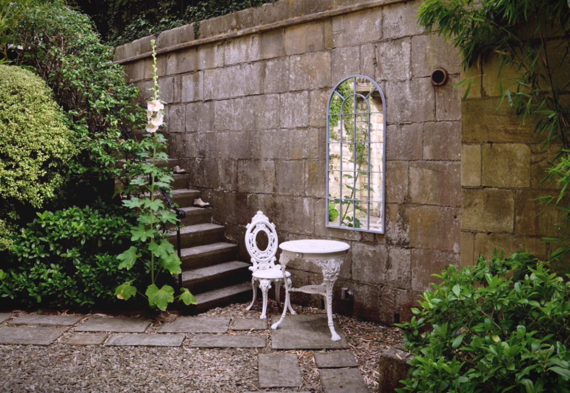 white patio furniture against a vine-covered wall with a mirror