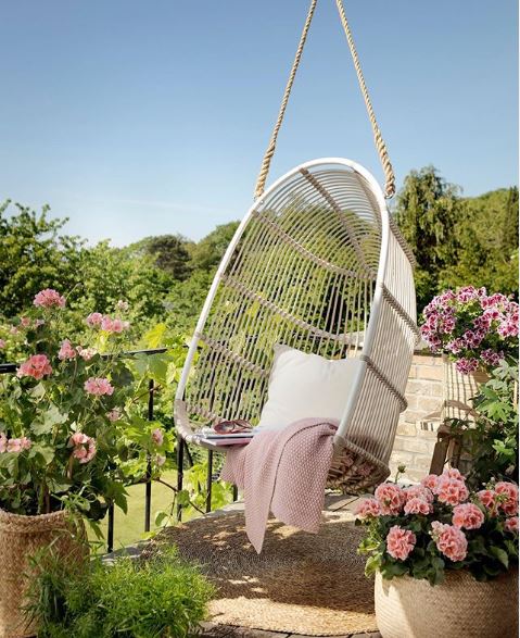 A beautiful suspended chair wth a pink blanket, surrounded by flowers