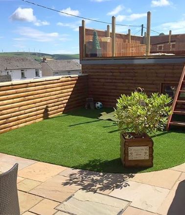A garden with a corner of artificial grass, the rest is paved and there are wooden steps leading to an upper level.