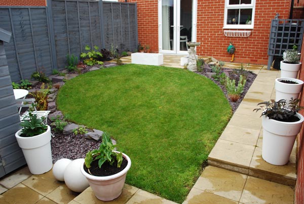 A small garden with a tidy flower bed, lawn and several big white planters