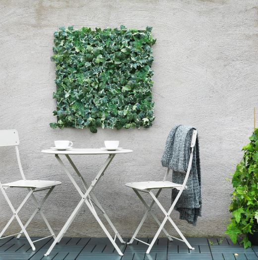 A white bistro set on a deck against a wall with artificial plant tiles