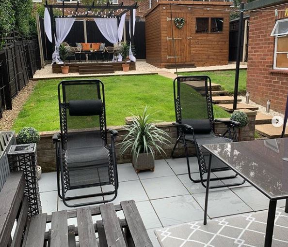 A manicured garden with a pallet bench, reclining loungers, a dining table and outdoor sofa