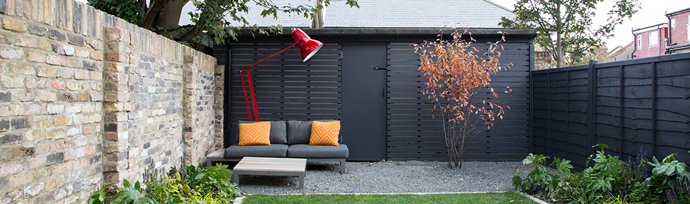 a giant adjustable Anglepoise lamp sits behind a garden sofa on a patio in front of a shed