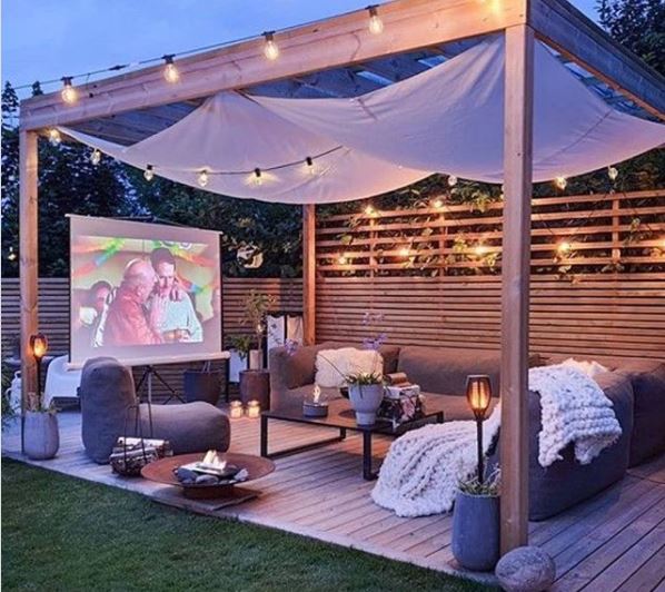 Cosy garden cinema set up under a pergola with festoon lighting
