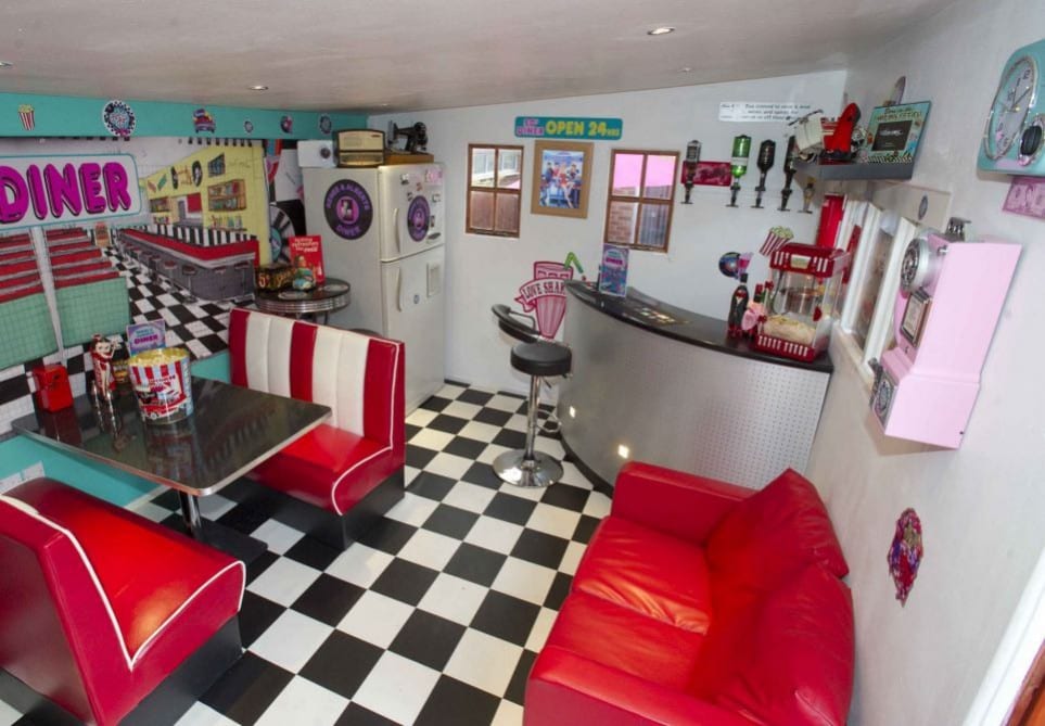 the interior of a shed made to look like a 1950's diner with red vinyl seats, a checkered floor and a corner bar