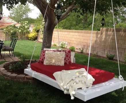 A DIY platform with a red futon and cream cushions hangs from a tree