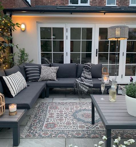 Dark slimline furniture on a patio with a rug, outdoor lamp and fairy lights 