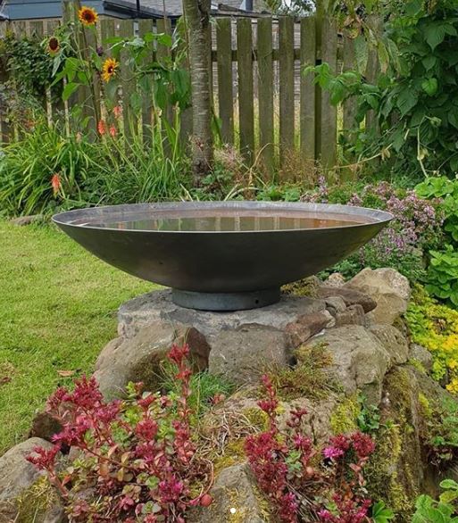 Japanese style water bowl on a stone plinth in a busy garden