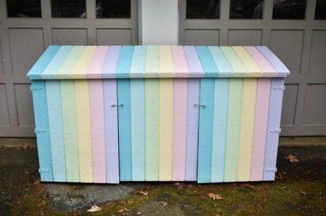 An outdoor bin store unit that's been painted in pastel rainbow shades to be used as toy storage