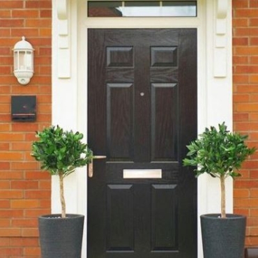 Two artificial bay trees stand either side of the front door to a new-build home, painted a smart black.
