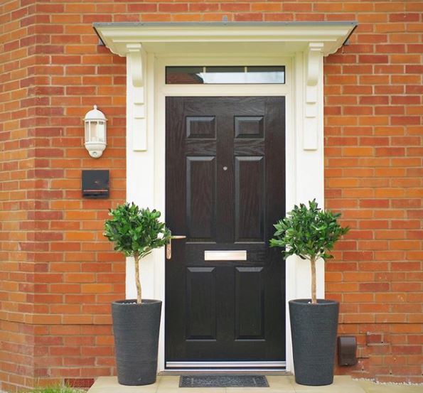 Two artificial bay trees stand either side of the front door to a new-build home, painted a smart black.