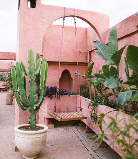 A simple wooden swing hanging from an archway in a moroccan inspired garden