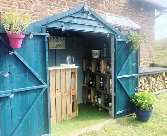 a blue garden shed with a pallet bar inside and alcohol bottles stacked on DIY shelving