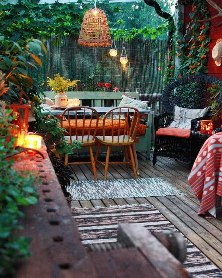 a boho style garden with a narrow table at the far end in front of a fence that lets you see the trees on the other side