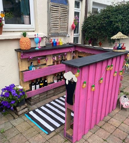 a bright pink pallet bar with multicoloured accessories like plastic wine glasses and novelty fairy lights