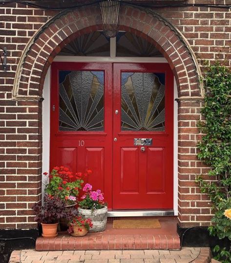 a bright red front door with shining hardware, and plant pots to one side