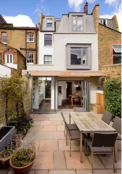 a courtyard with subtle rectangular shapes in the table, chairs, paving stones, fencing, planter and architecture.
