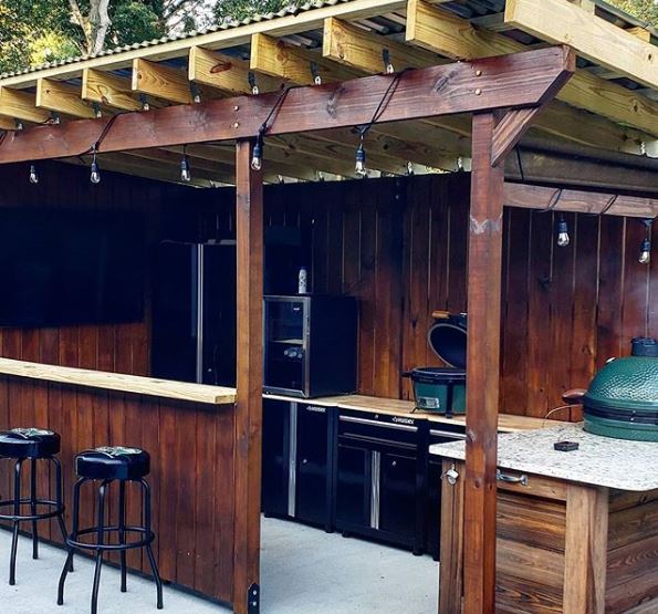 a covered patio area with outdoor kitchen appliances and a bar counter with stools