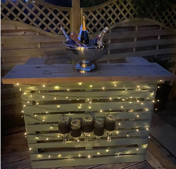 a deck with a pallet bar that has fairy lights strung around it