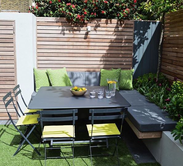 the corner of a modern garden with in-built benches and folding metal chairs