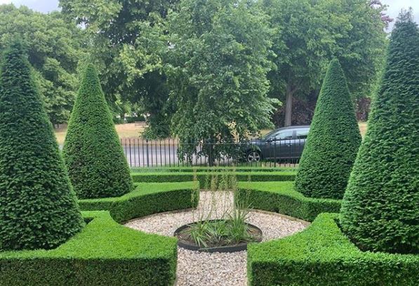 a front garden with an intersection of gravel paths through tall conical topiary trees