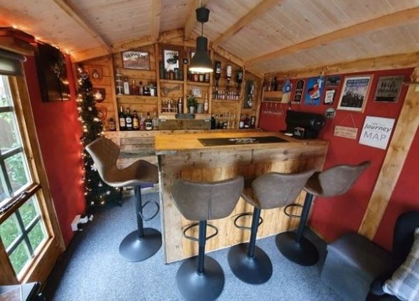 a garden shed transformed into a home pub, with bar stools and fully stocked drinks shelves