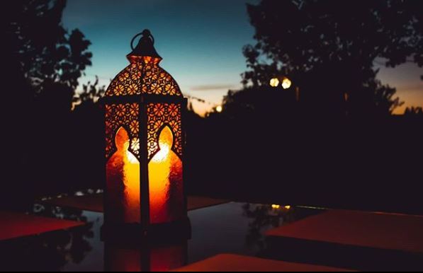 a moroccan lantern with a burning candle inside, on a table, at dusk