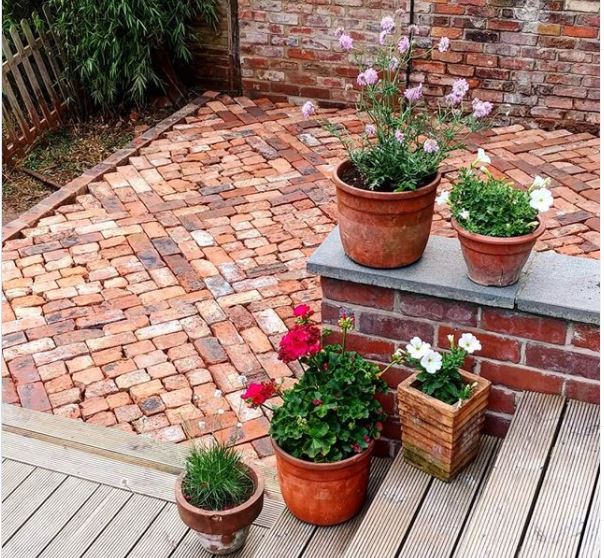 a patio made from vintage bricks next to a deck with potted plants