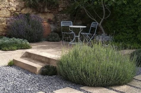 a raised stone patio with furniture, in a gravel garden with several huge lavender shrubs