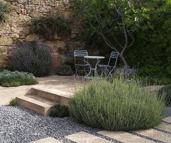 a raised stone patio with furniture, in a gravel garden with several huge lavender shrubs