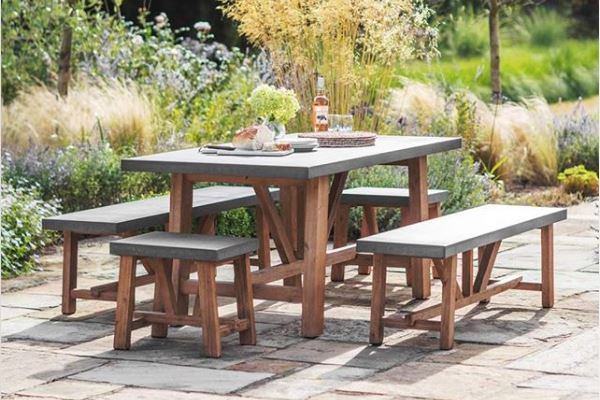 a set of benches and dining table with wooden frames and concrete tops on a rustic flagstone patio