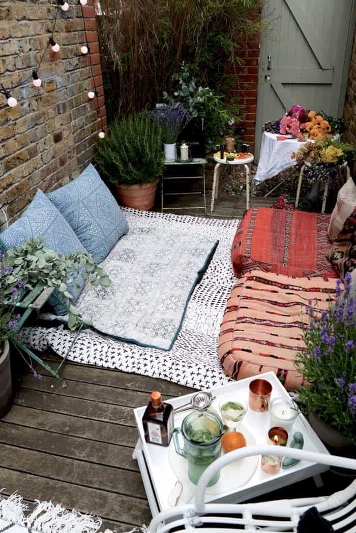 a small bohemian courtyard with blankets on the floor and large cushion seats