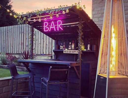 a small garden bar with pink LED neon light that reads BAR and a patio heater