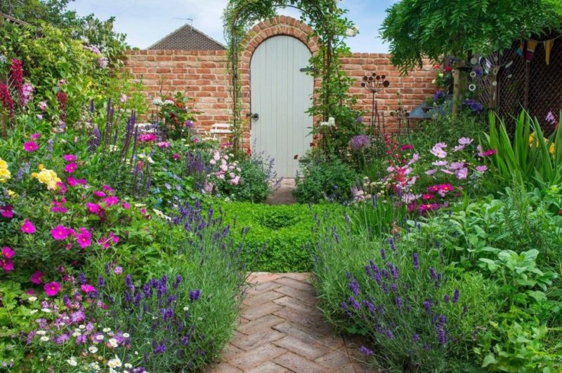 25 English Cottage Garden Ideas: Capture the Fairytale Charm 7 a small garden with overflowing flower beds and a brick path leading to a pretty gate at the end