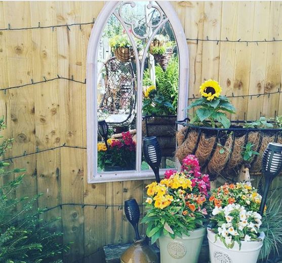 a small mirror shaped like a gothic window, reflecting colourful pots and flowers