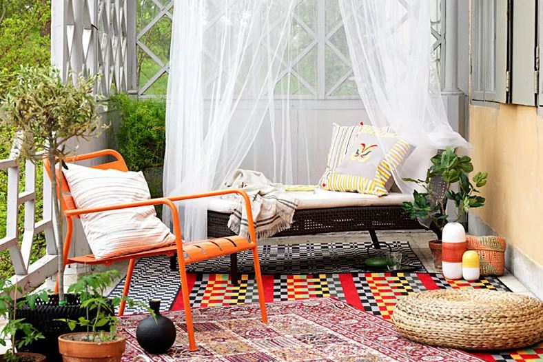a small terrace with a bright orange chair, loud, clashing rugs and a day bed beneath a white net canopy