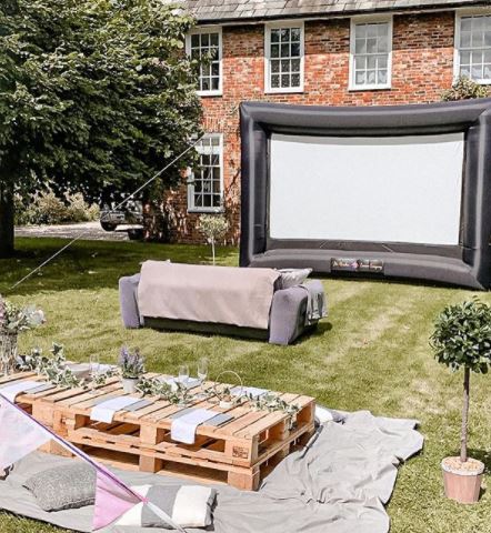 a sofa and pallet coffee tables in front of a large inflatable cinema screen