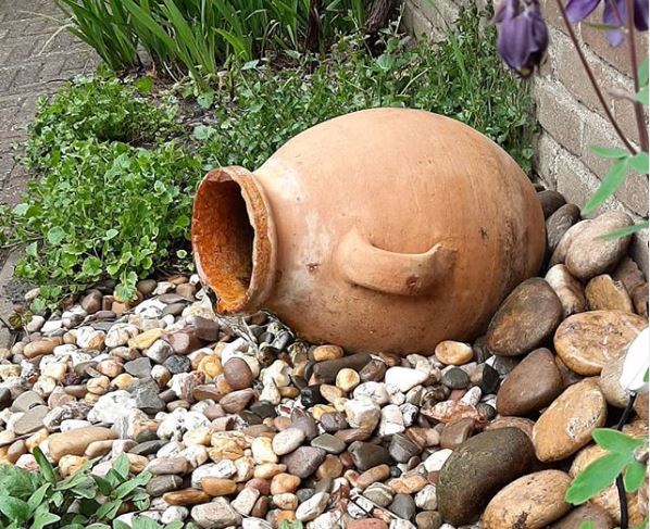 greek garden ideas with a terracotta amphora on its side in a gravel flower bed