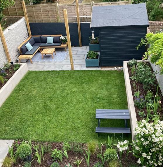 a well-laid out garden, with flower beds, a lawn with a picnic table, and a patio with sofa seating and a shed