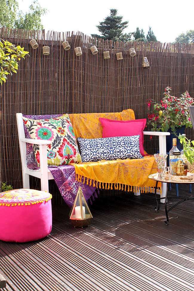 a white wooden bench with coordinated cushions in mustard yellow, hot pink, bright purple and deep blue