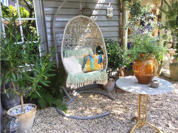 a wicker suspended chin hanging in a graevl garden surrounded by potted plants