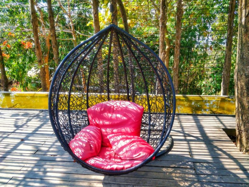 an ornate black swing chair with squashy red cushions on a deck
