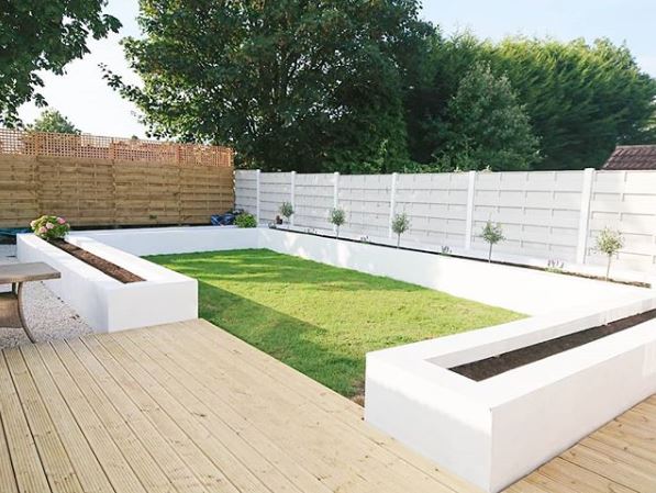an organised garden with rectangluar lawn, wooden deck and long raised planters painted white