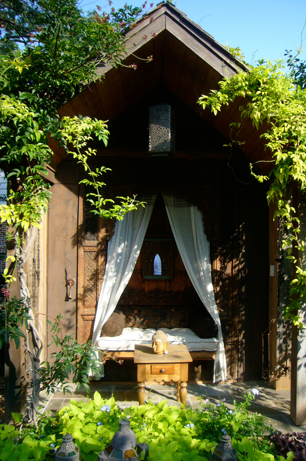 an outdoor day bed beneath a wooden roof and curtain canopy