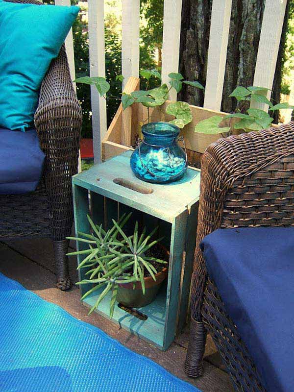 an upended crate, painted blue, being used as a side table for a plant and decorative blue vase, between two wicker chairs with blue cushions