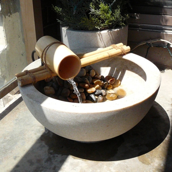 a small DIY bamboo water feature, with a trickle falling into a pebble-fulled bowl beneath