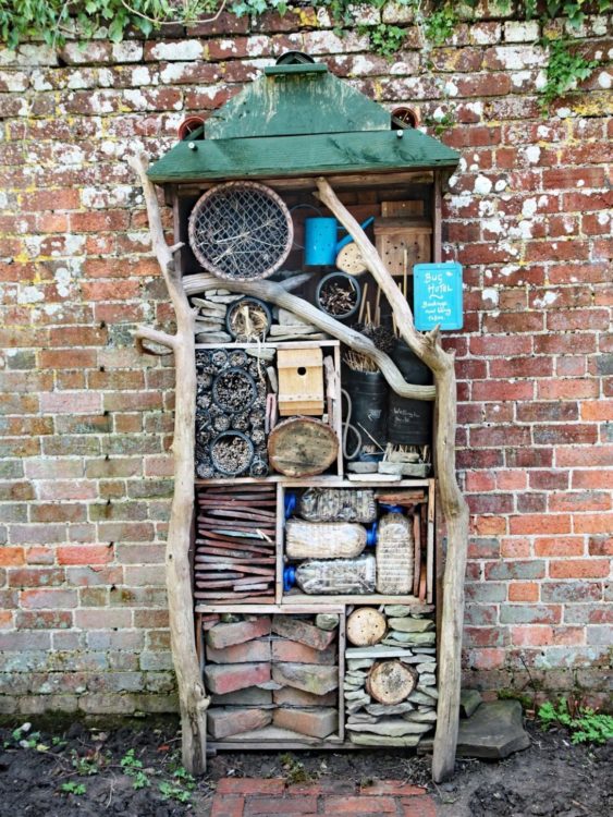 a tall, rustic insect hotel made from branches and garden debris