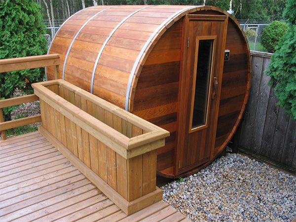 a cedar barrel sauna next to a wooden deck in a garden